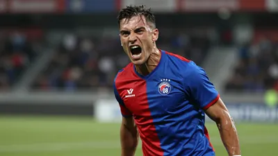 A mid-30s Sarpsborg 08 forward, muscular, sweat-glazed skin, head turned toward the camera, eyes fierce, mouth open in a...